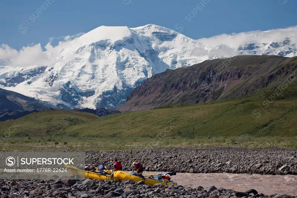 Group of people rigging for a raft trip near the headwaters of the Jacksina river with Mt Jarvis behind, Wrangell_St. Elias Nati