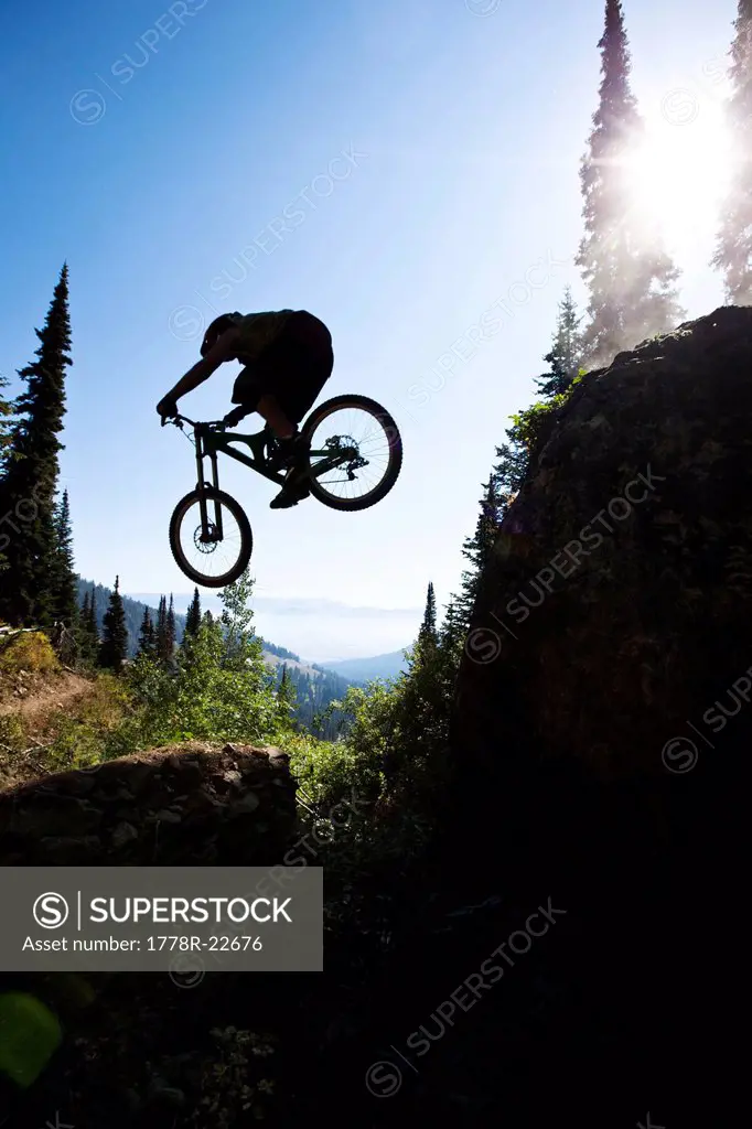 A athletic man mountain biking jumps off a large cliff while downhilling in Wyoming.