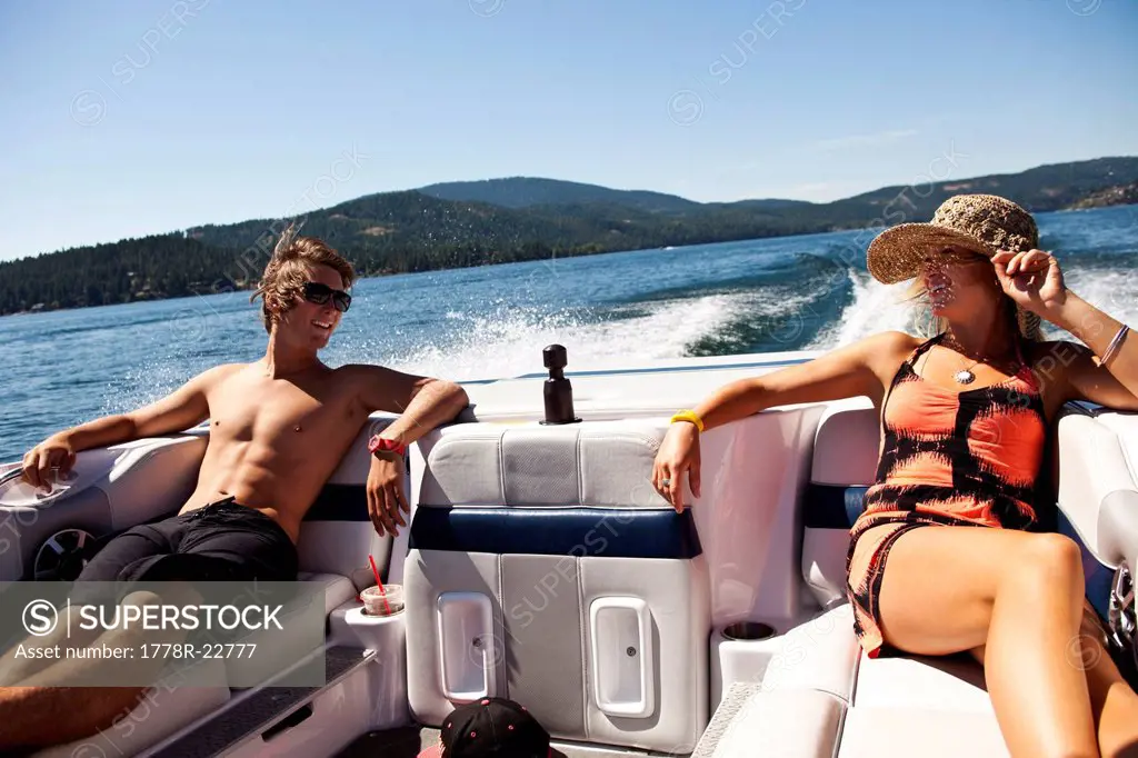 Two happy young adults laughing and talking on the back of a wakeboard boat on a sunny day in Idaho.