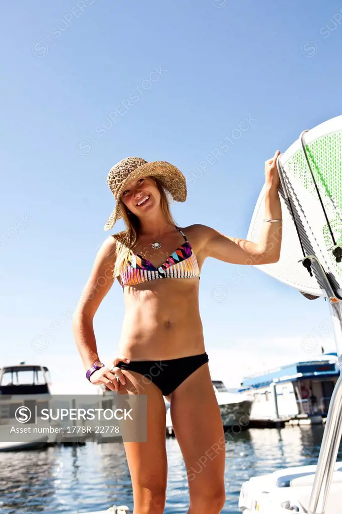 A athletic young woman smiles while standing next to a wakeboard boat in Idaho.