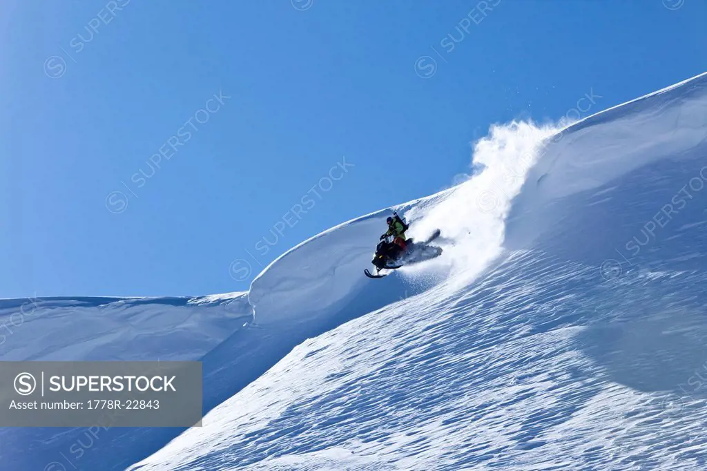 A snowmobiler jumping off a cornice on a sunny winter day in Montana.