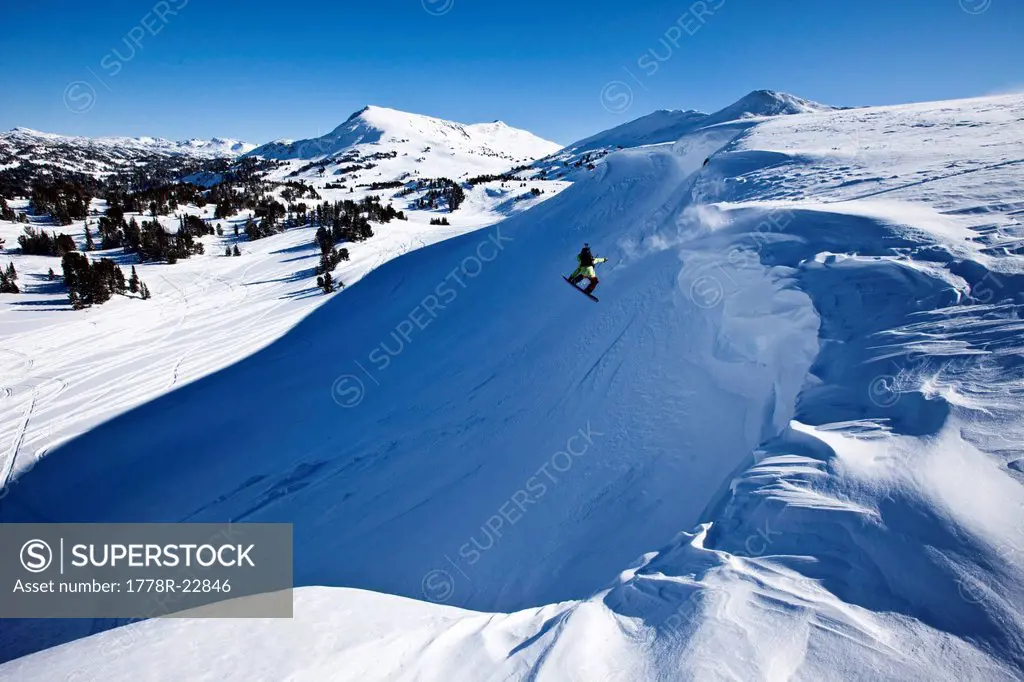A snowboarder jumping off a cornice on a sunny winter day in Montana.