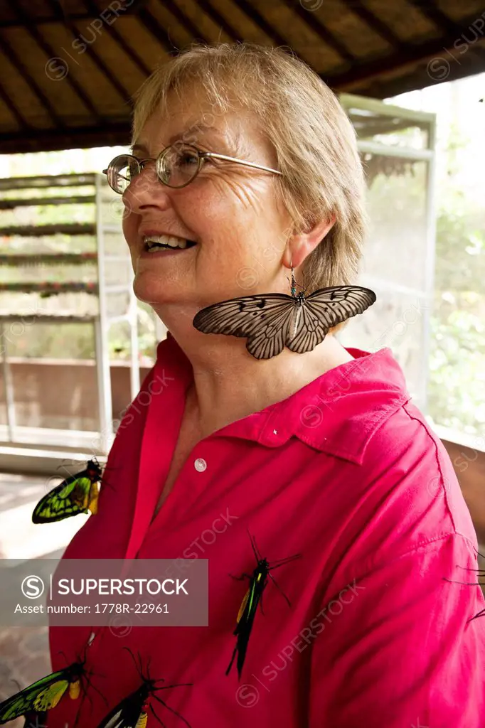 A retired woman smiling while covered in huge butterflies in Bali, Indonesia.
