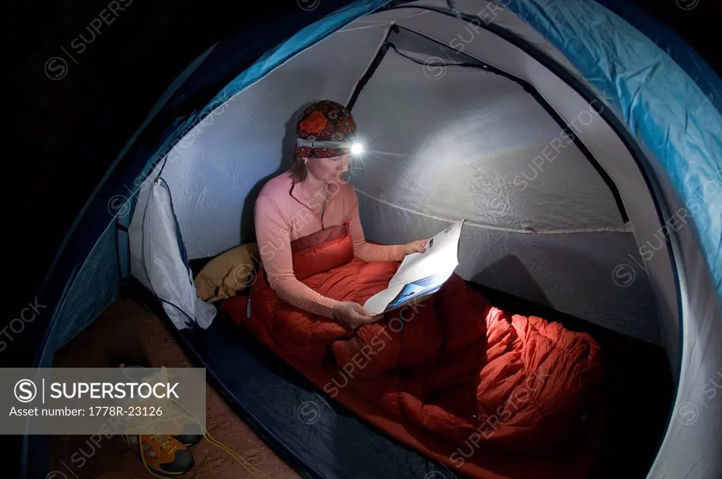A woman camping in a tent with a headlamp in Indian Creek Canyon, Monticello, Utah.