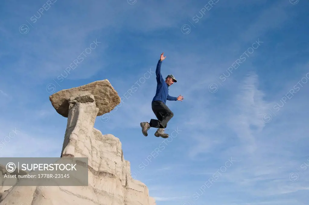 A man jumping off a sandstone rock formation, Bisti Badlands, Farmington, New Mexico.