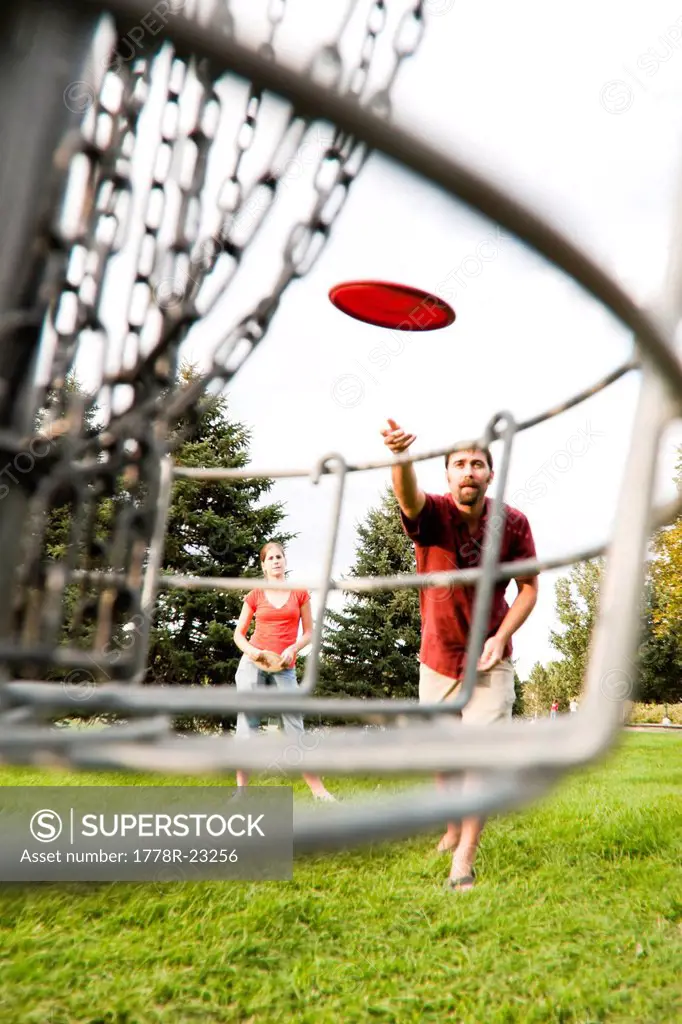A man and woman play disk golf.