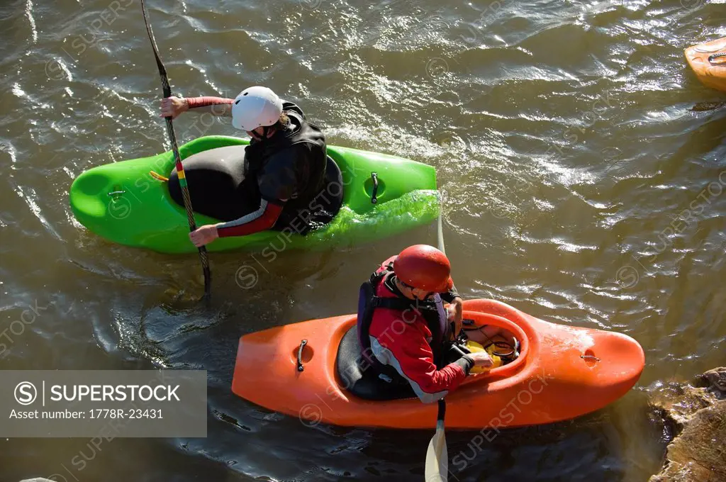 Two male whitewater kayakers float in an eddy.