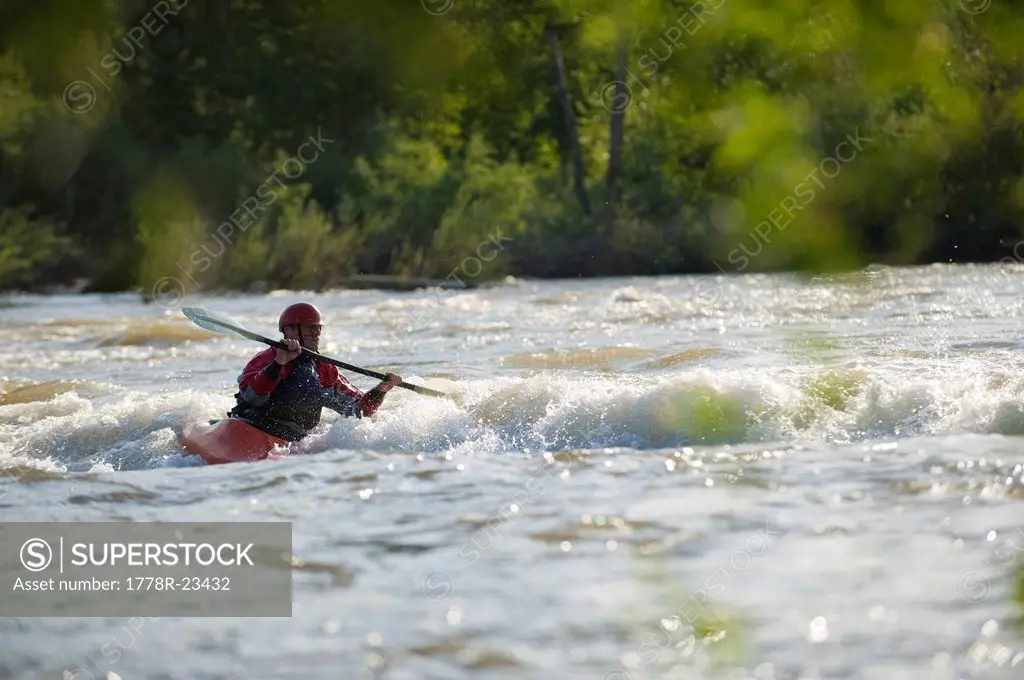 A male whitewater kayaker front surfs a wave.