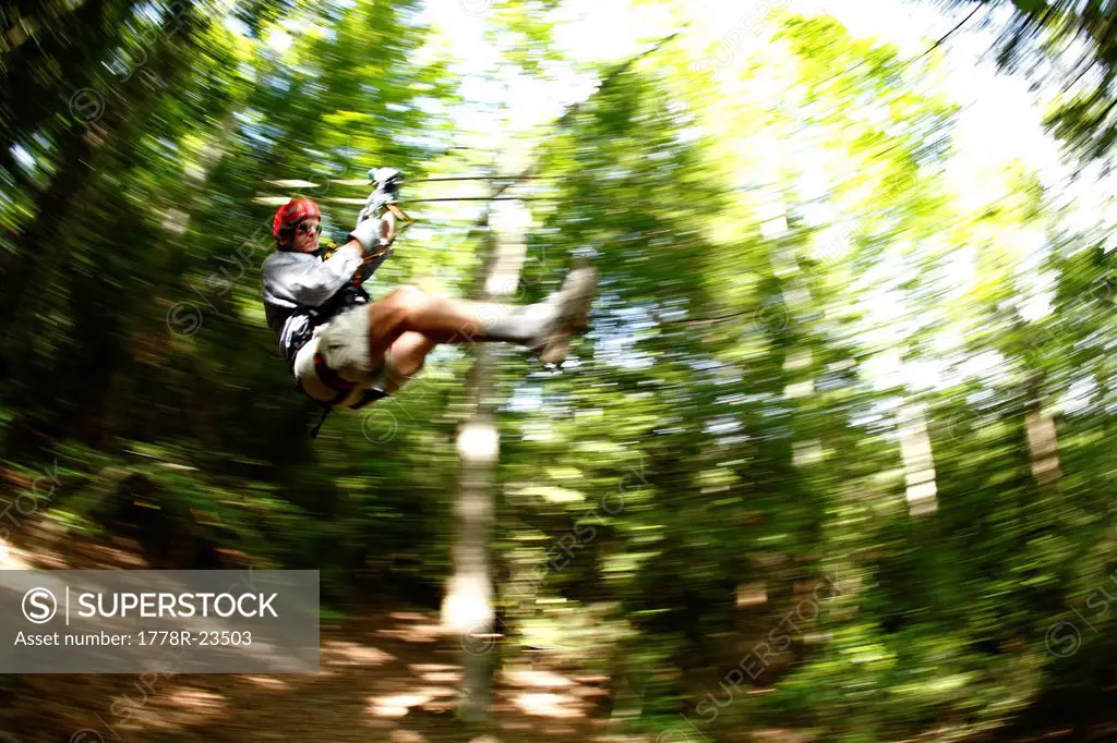 Pan_blur image of man on a zip_line in the tree canopy.