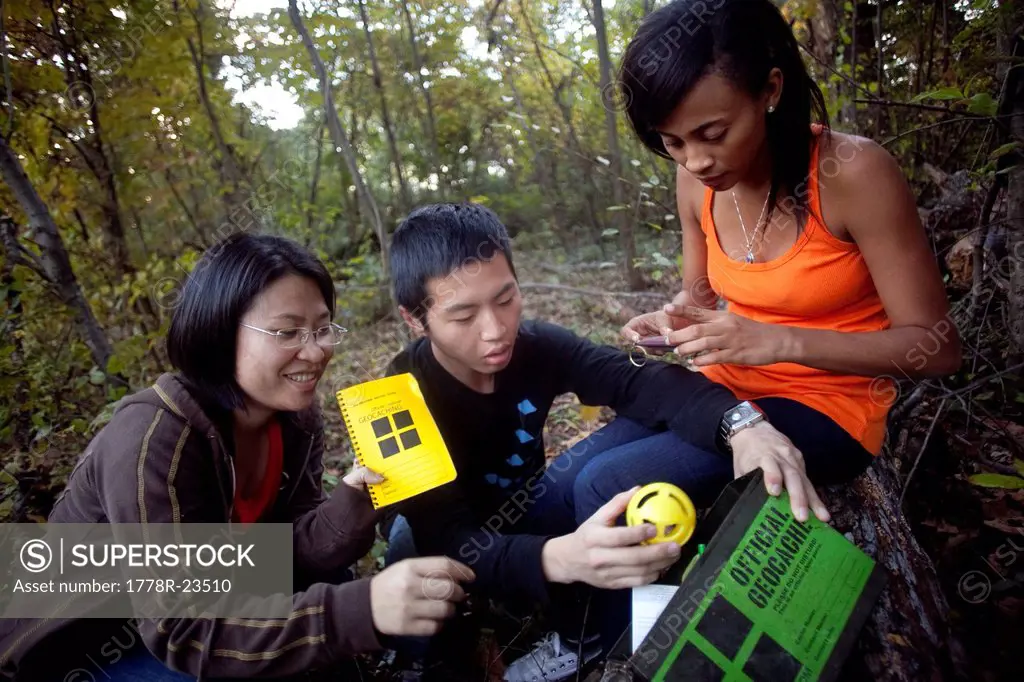 Three friends find a geocache in a park in Baltimore, Maryland.