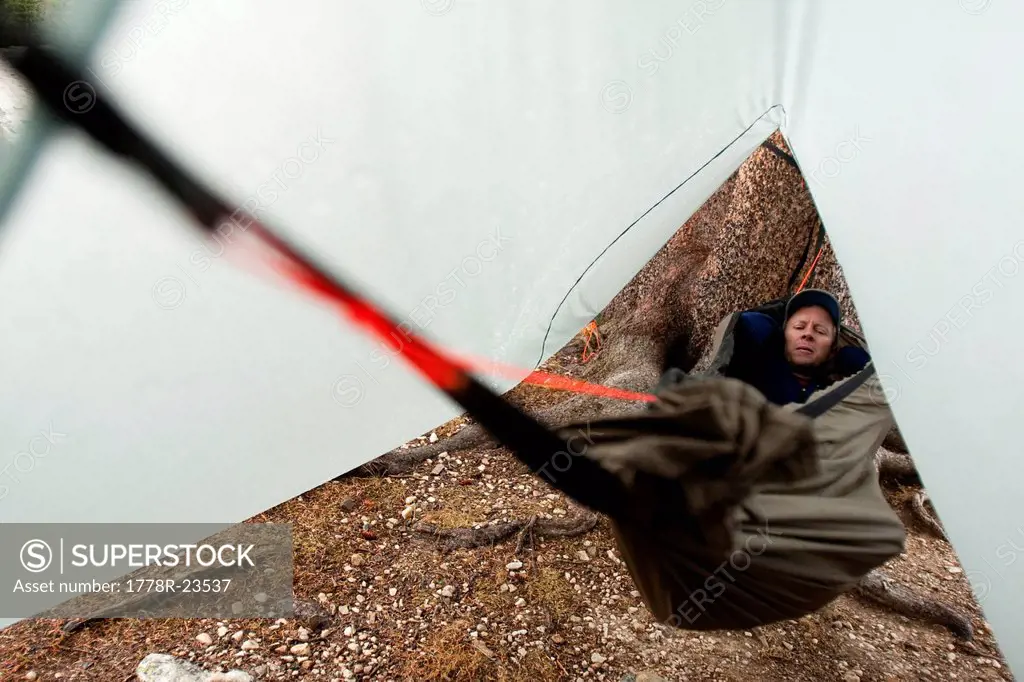 A man takes a short rest in a hammock with a rain fly during rainy weather in the Snowy Range, Wyoming.