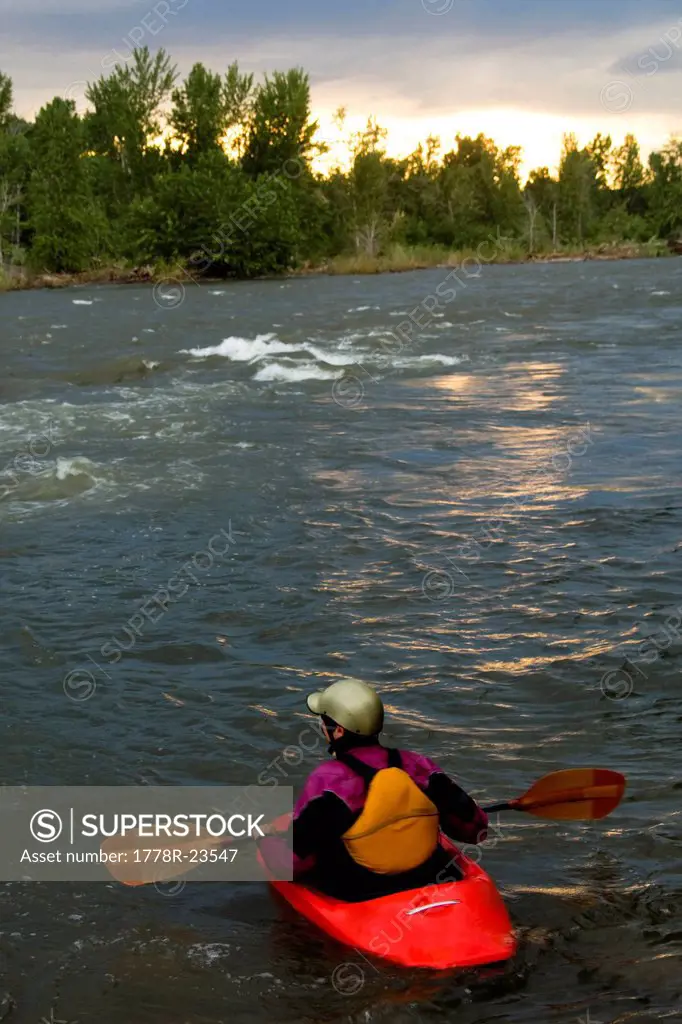A female kayaker in a playboat stops to watch the sunset in the Clark Fork River, Missoula, Montana.