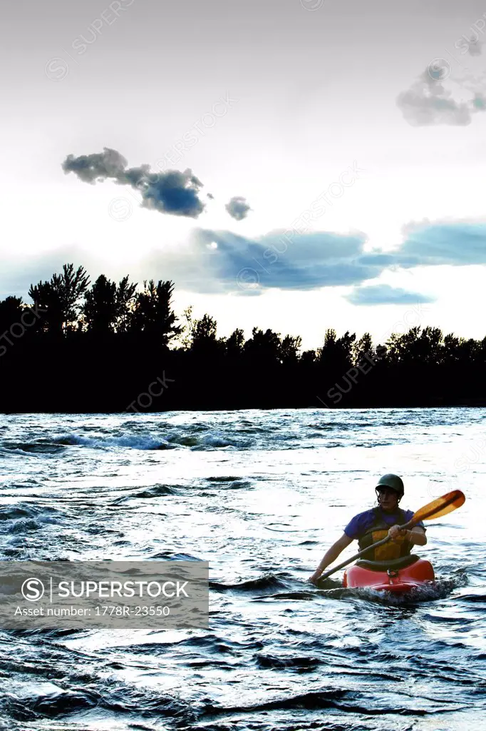 A female kayaker in a playboat paddles out at sunset on the Clark Fork River, Missoula, Montana.