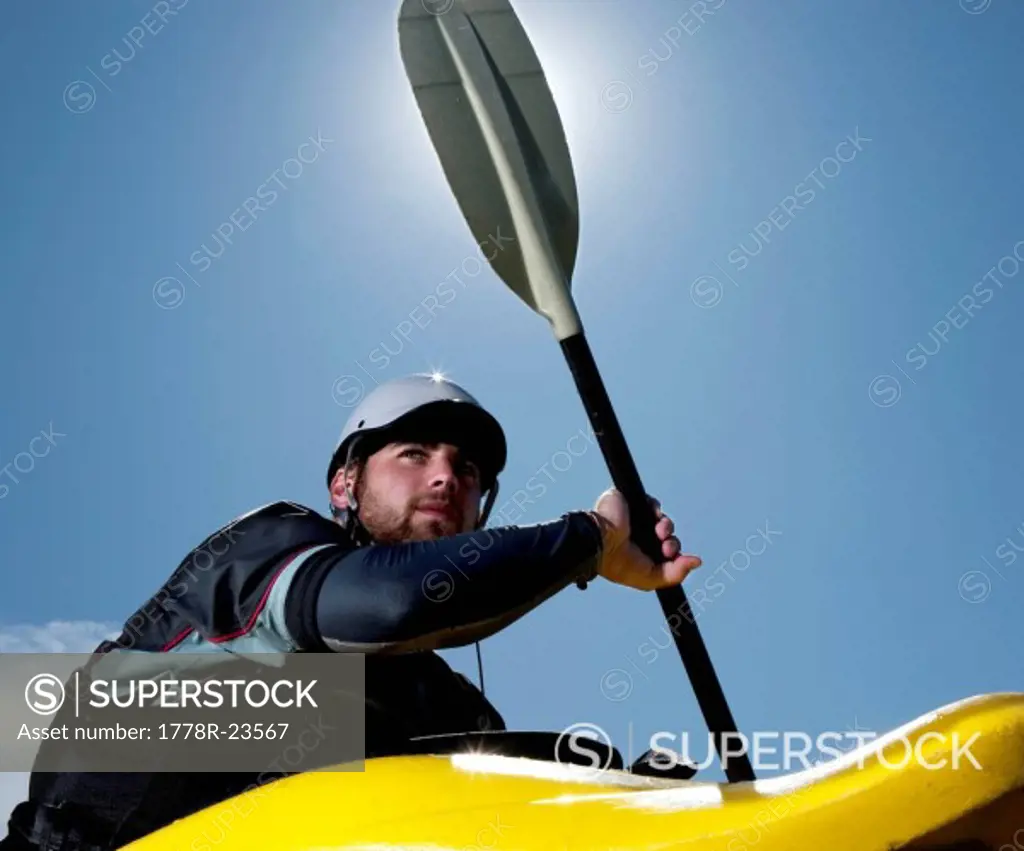 Low_angle view of a male kayaker in a playboat is backlit by the sun.