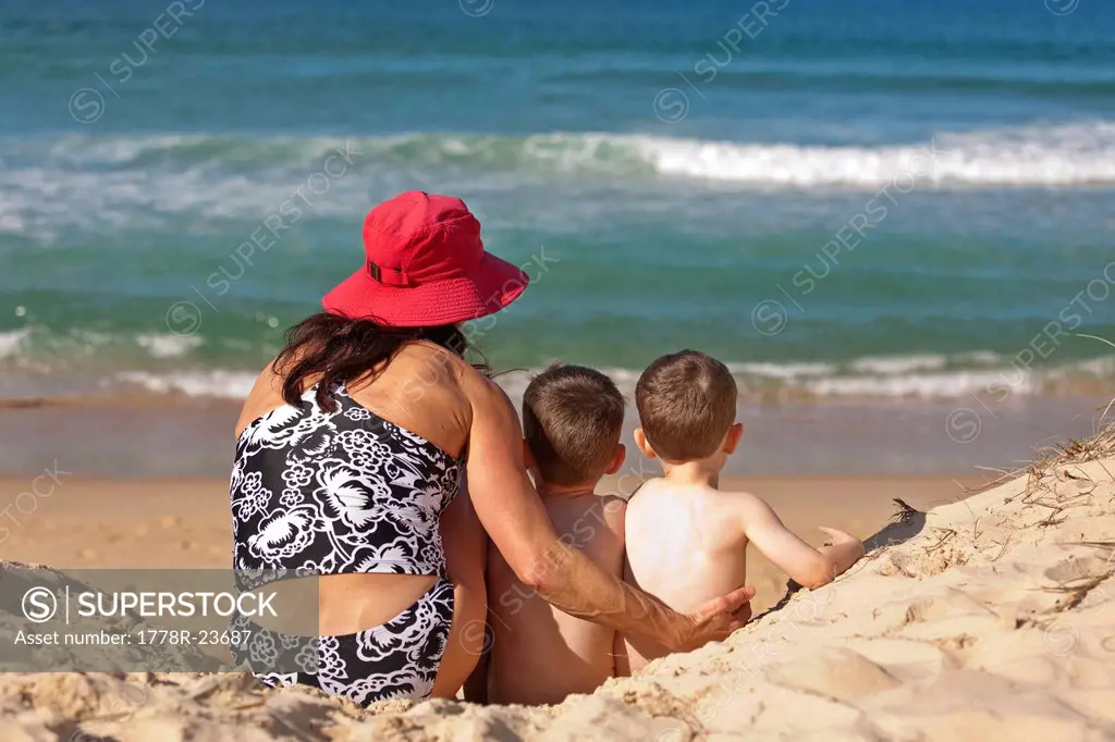 A woman and two children sitting on the sand at Sunshine Beach, Queensland, Australia.