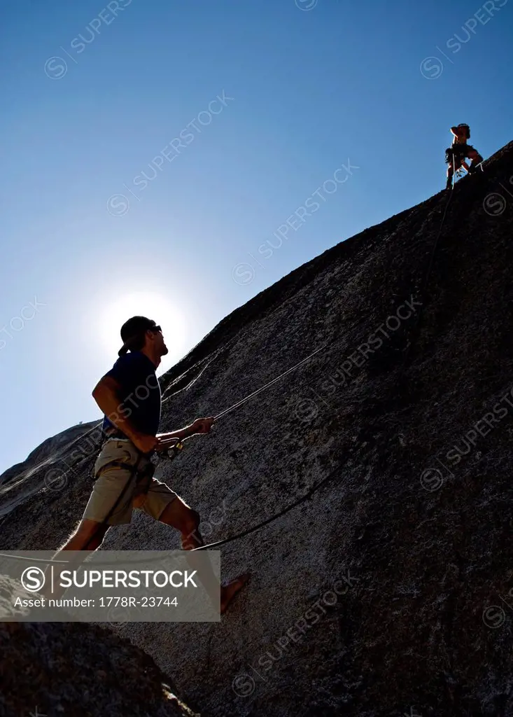A young man leads a rock climb, while another young man belays him, in Yosemite, California.