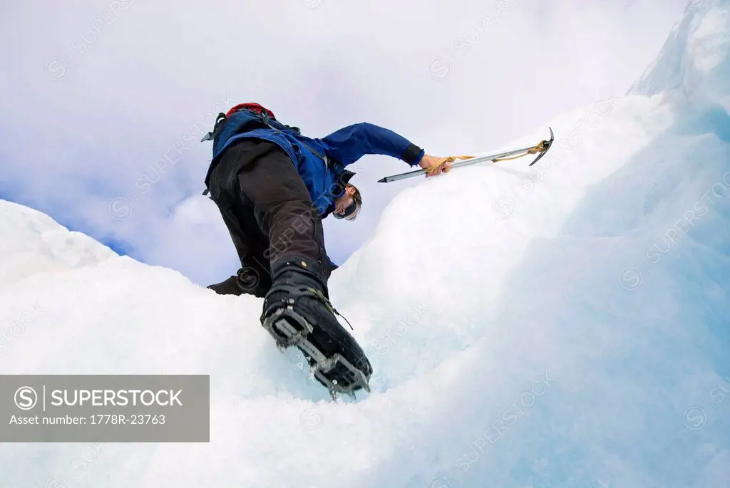 A young man climbs up steps on a glacier with crampons and an ice axe in Franz Josef, New Zealand.