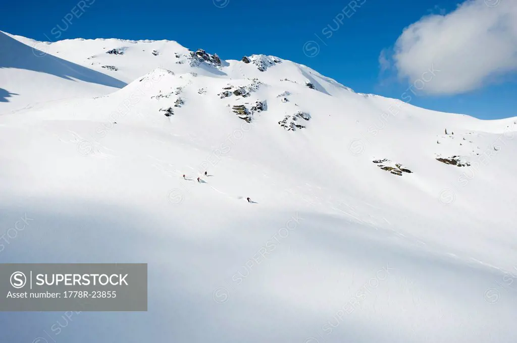 A group of skiers take a run down a large alpine bowl in the backcountry of the Selkirk Mountains, Canada.
