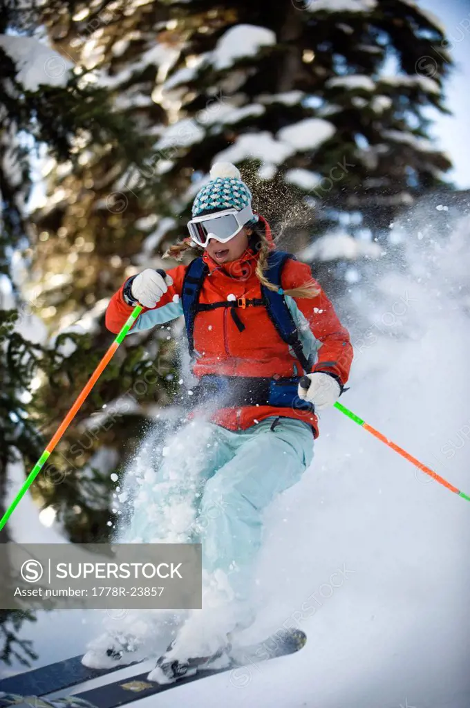 A woman backcountry skier catches air in the trees of the Selkirk Mountains, Canada.