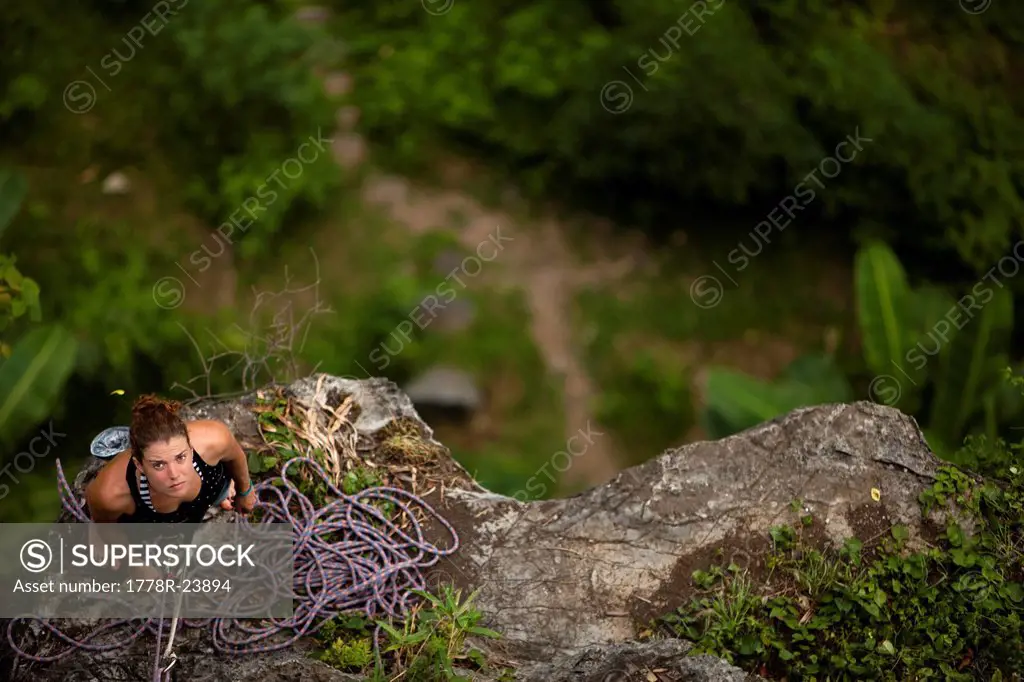 Caucasian female climer looking up from belay station 60 metres above in rural Asia.