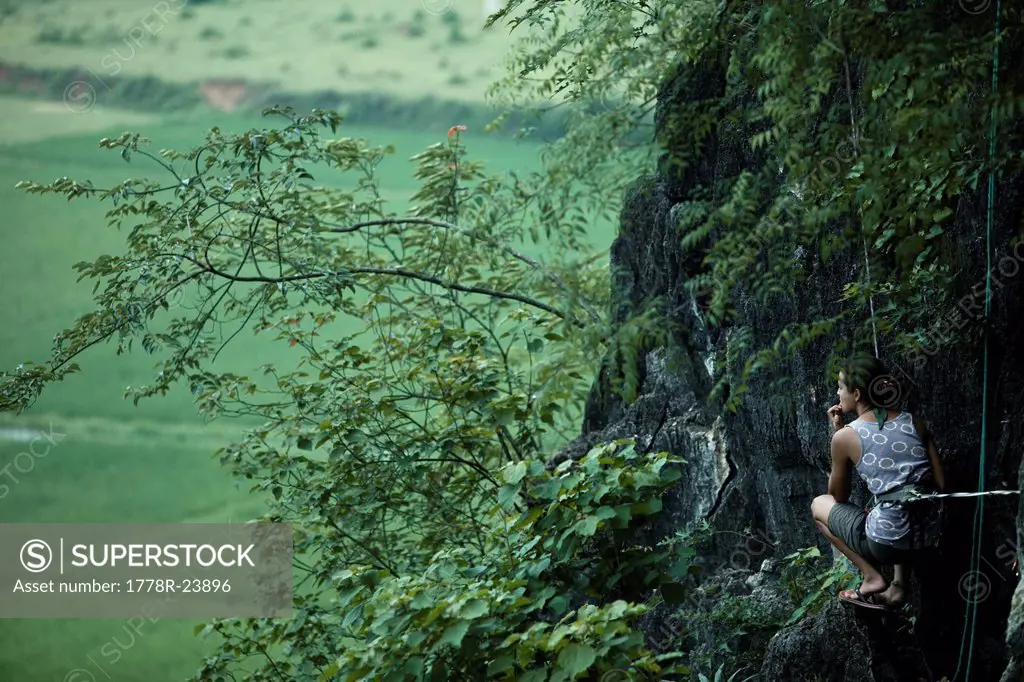Caucasian female climber perched on her heels, belaying, looking contemplative.