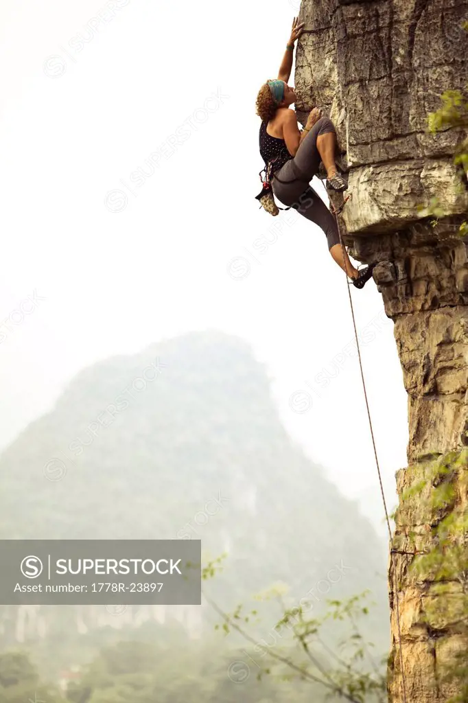 Female climber reaching out for a distant hold on overhanging limestone in China.