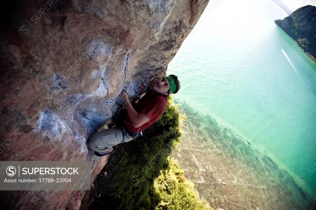 Strained male climber looks to his next move on a limestone beach cliff in Thailand.