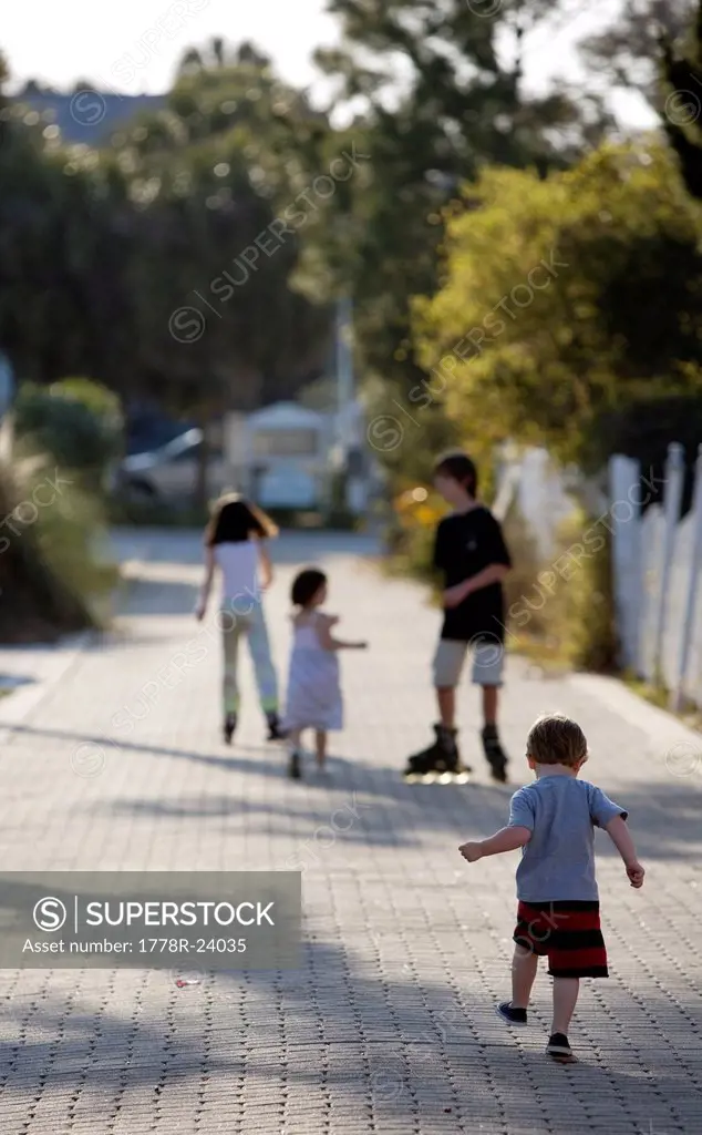 A group of kids are roller blading and walking down an alley.
