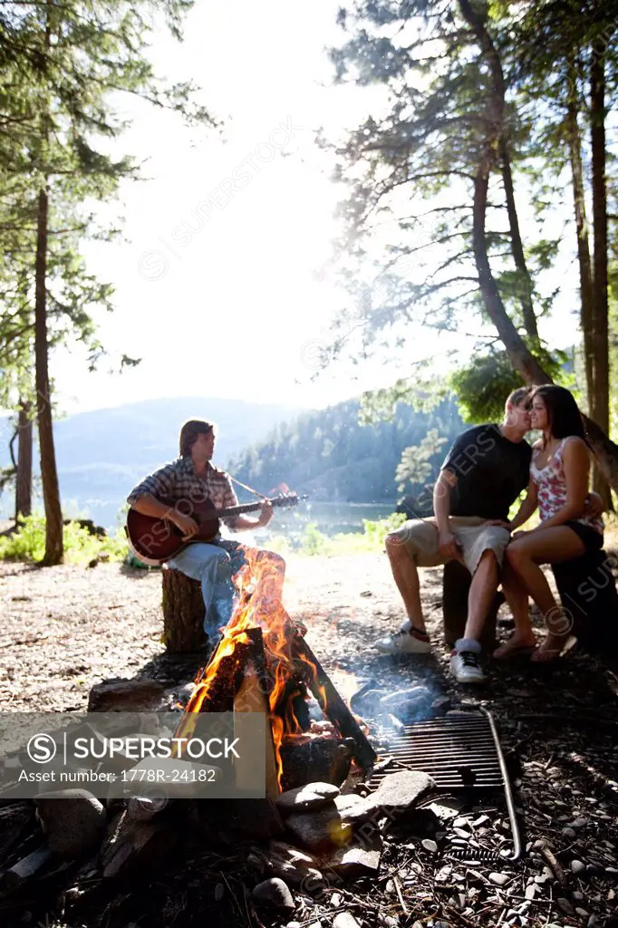 Young adults camping sit around a fire next to a lake in Idaho.