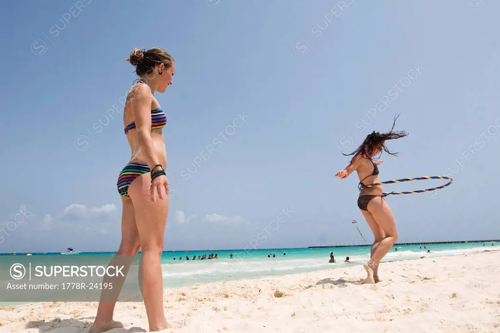 A girl watches as her friend is hula hooping on the beach in Mexico.