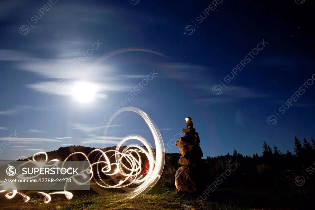 Rock cairn with light painting next to it and full moon in background in Idaho.