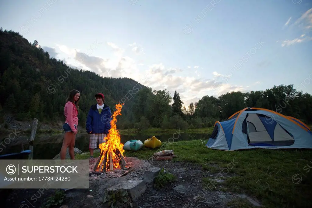 Young adult couple camping with a camp fire and kayaks on a beautiful summer evening.
