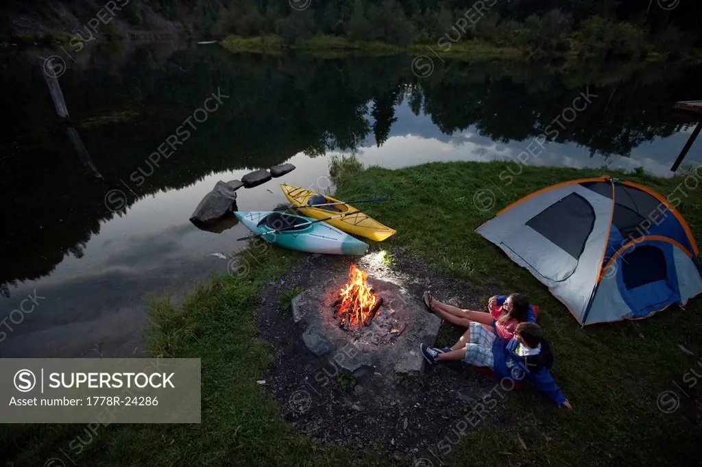 Young adult couple camping with a camp fire and kayaks on a beautiful summer evening.