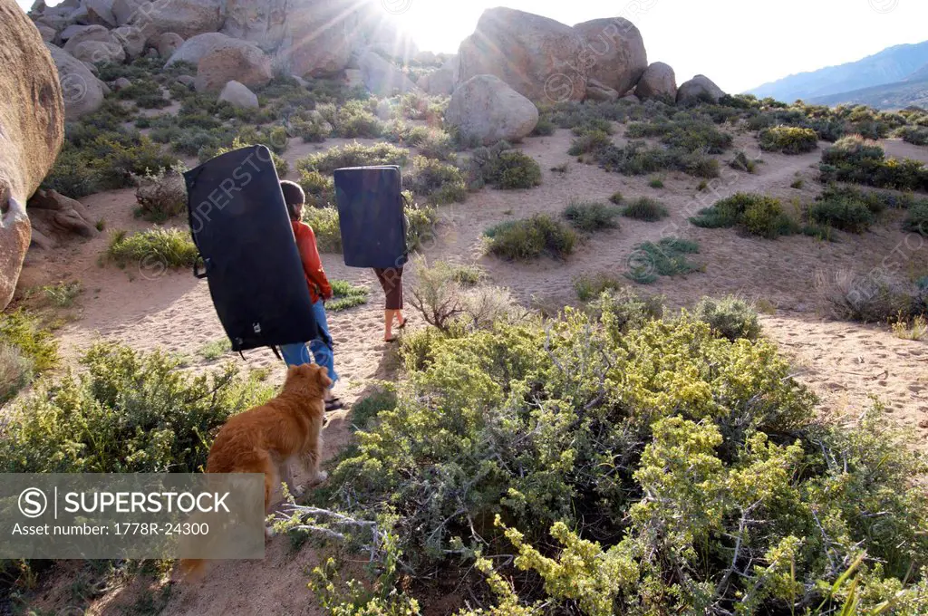 Two women and a dog hiking with bouldering pads at the Buttermilks, California.