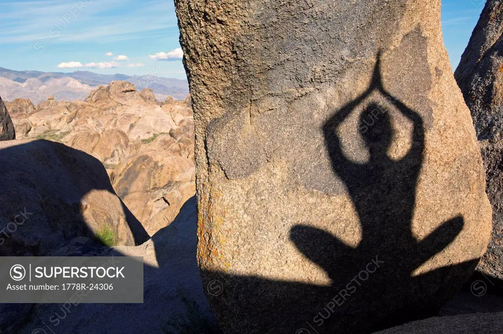 A shadow on a boulder of a woman practicing yoga.