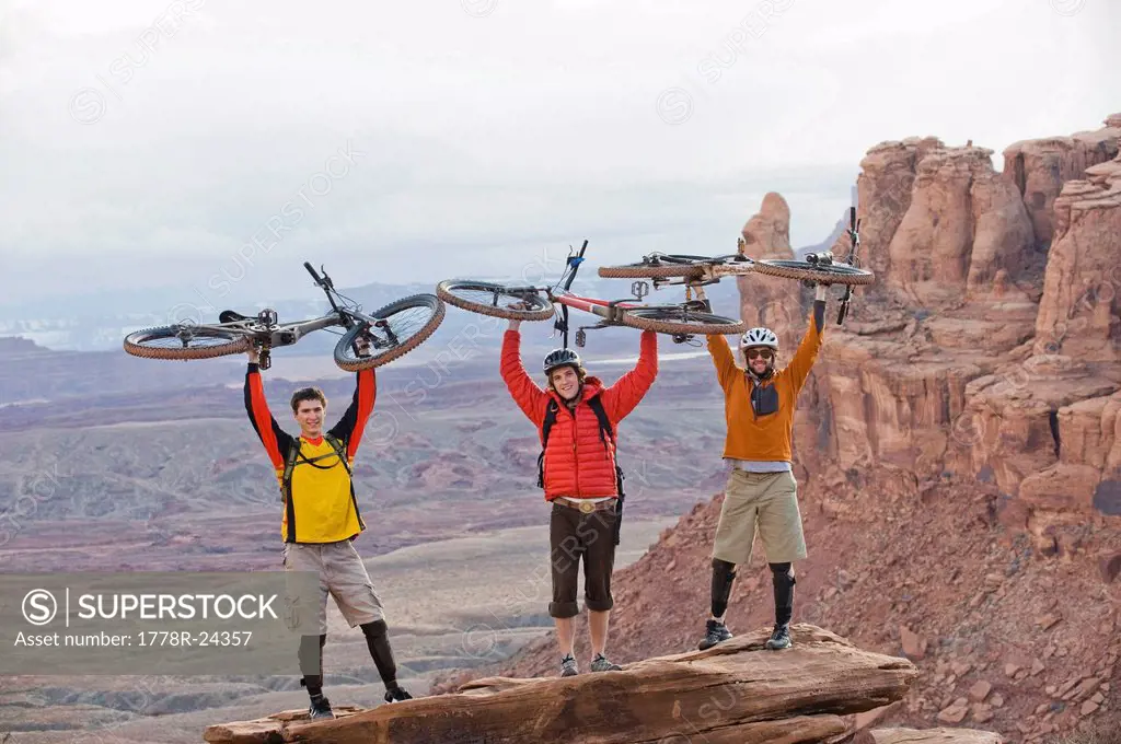 Three young men hold their bikes over their heads on the Amasa Back Trail, Moab, UT.
