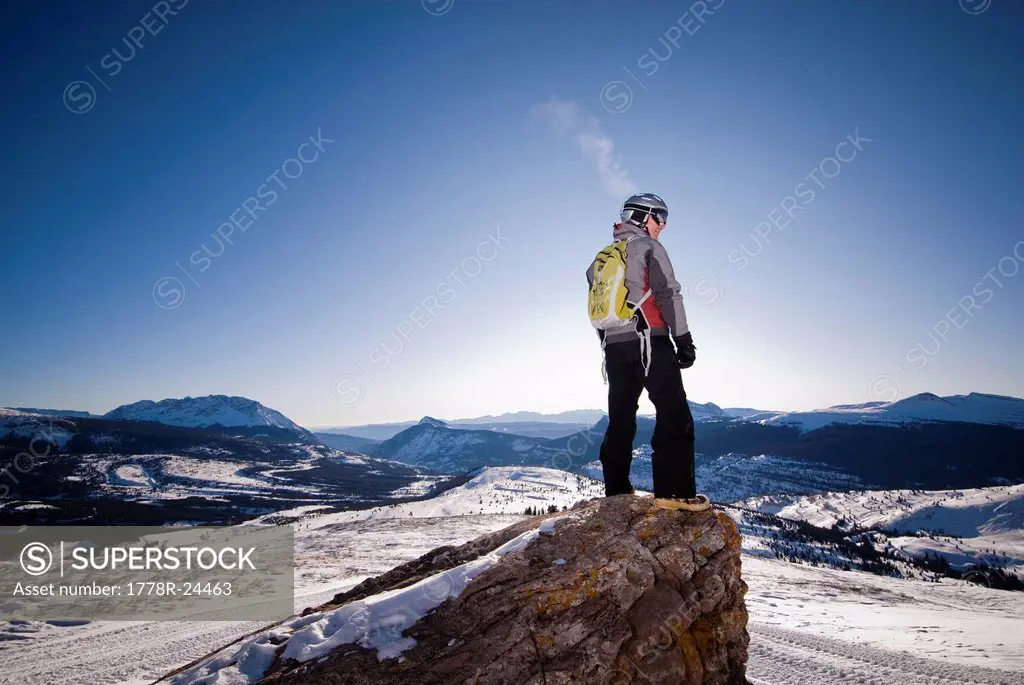 A middle aged man looks into the distance over a valley of snow in the Rocky Mountains.