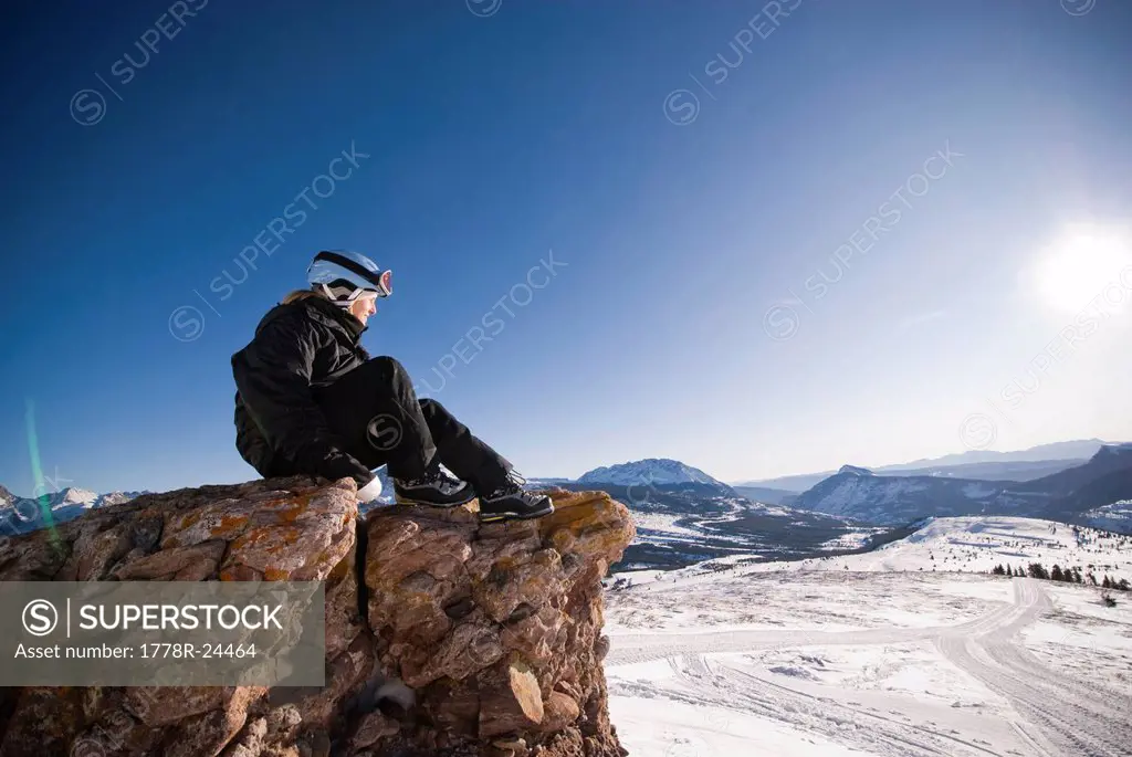 A middle aged woman looks into the distance over a valley of snow in the Rocky Mountains.