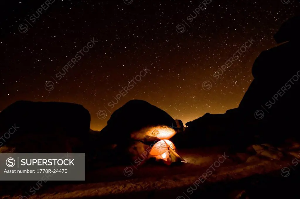 A tent illuminates the night with a star filled sky.