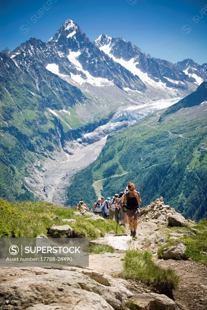 Hikers trek up a hill as the majesty of the Alps towers in the background.