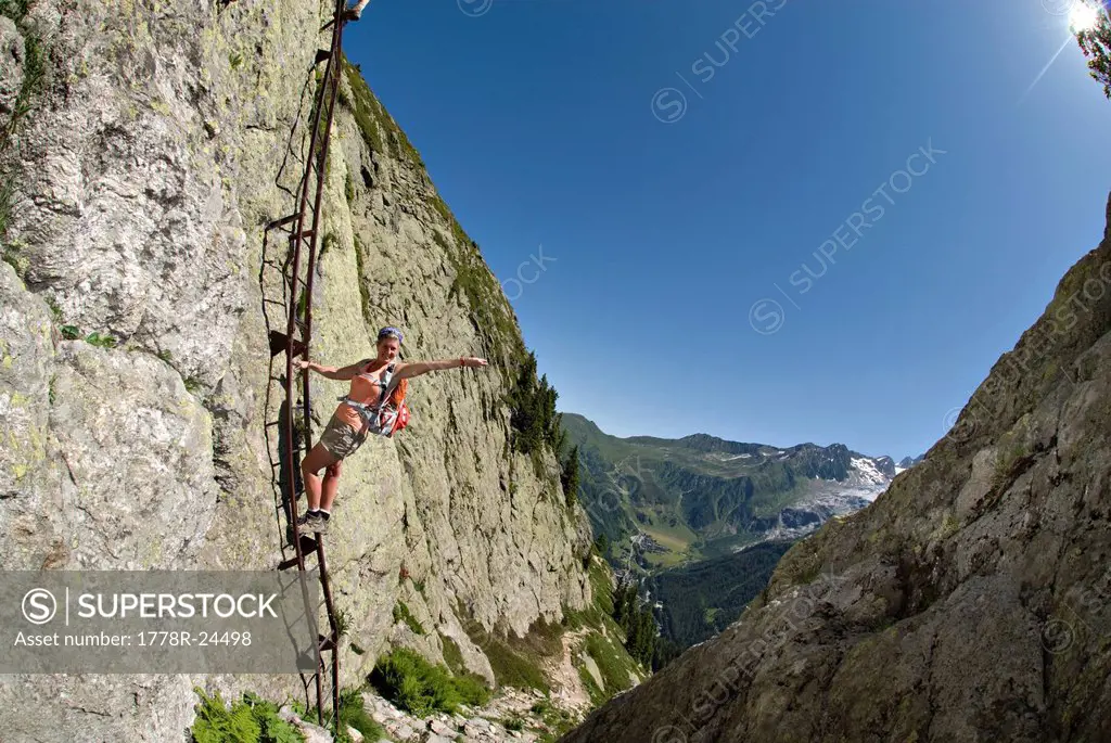 A youg woman poses on a ladder bolted to a large cliff face in the Swiss Alps.