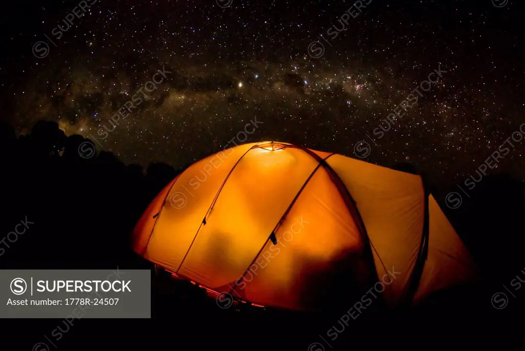 A tent illuminates the night as the Milky Way Galaxy floats above in a starry sky on Mt. Kilimnajaro.