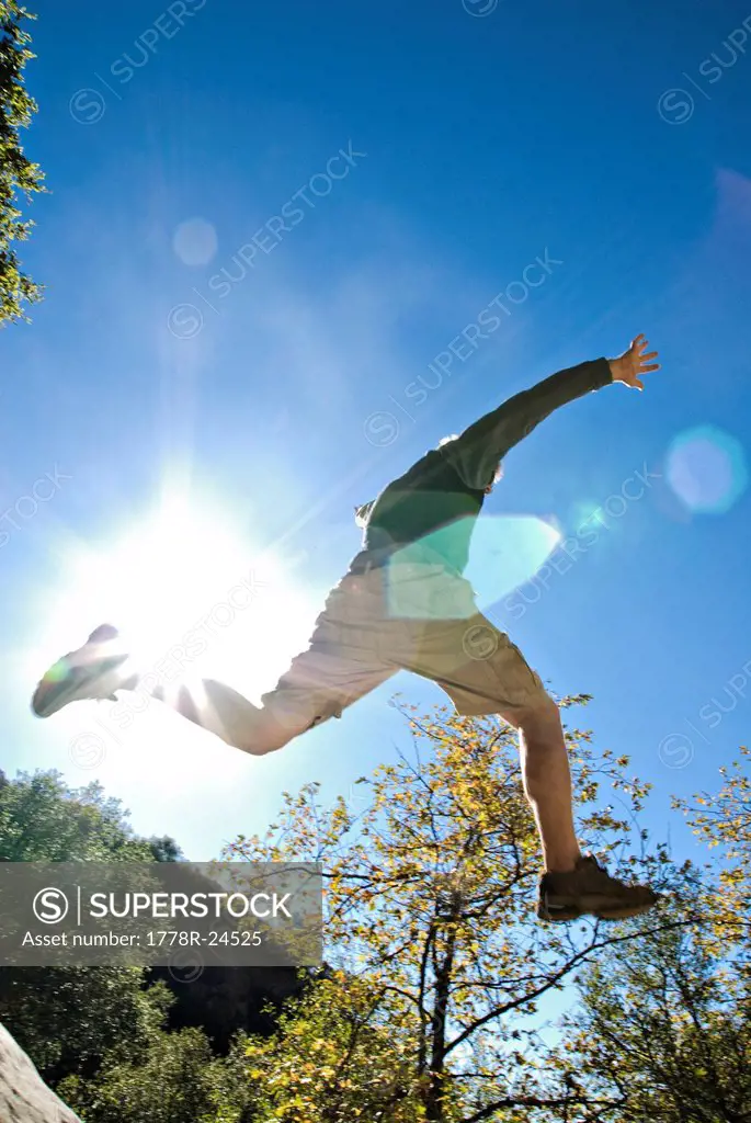 A young man jumps off of a rock while hiking a trail.