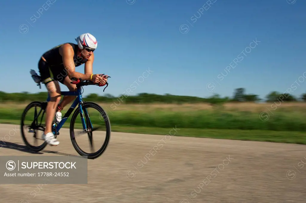 A male athelete training for a triathlon at a lake on a bike.