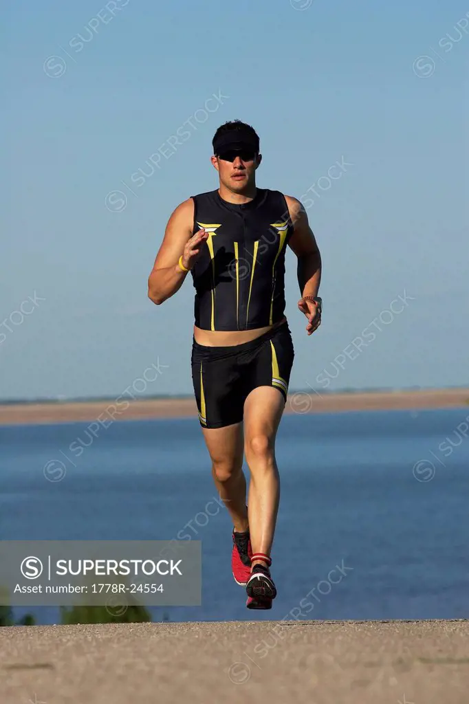 A male athelete running while training for a triathlon at a lake.