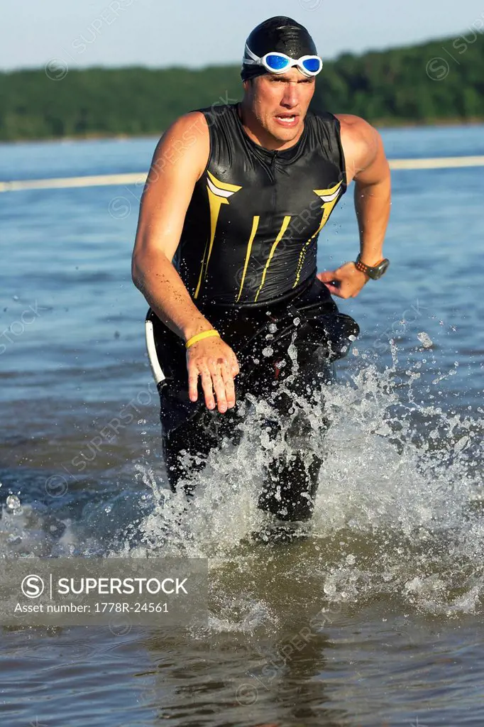 A male athelete running out of the water while training for a triathlon.