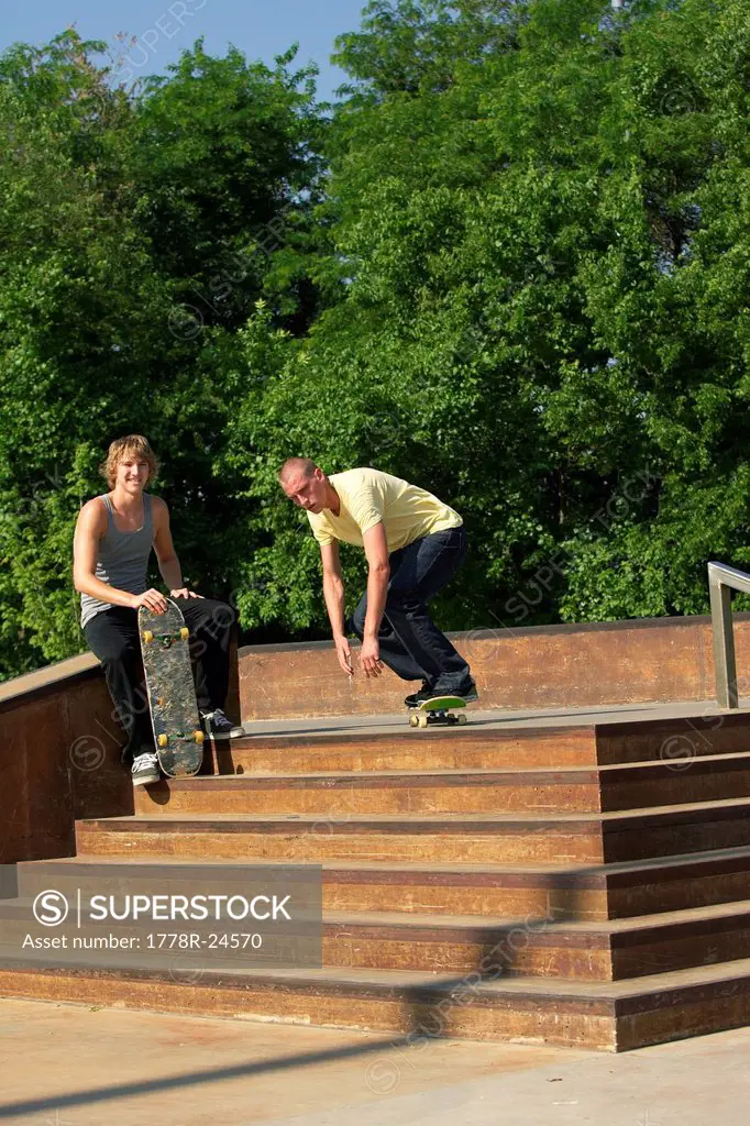 Two male skateboarders doing tricks at skate park off stairs.
