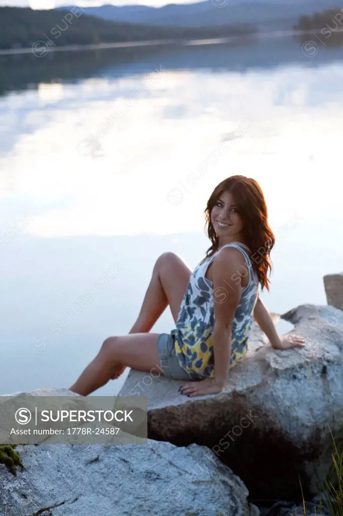 Young woman smiles while sitting next to the lake at sunset.