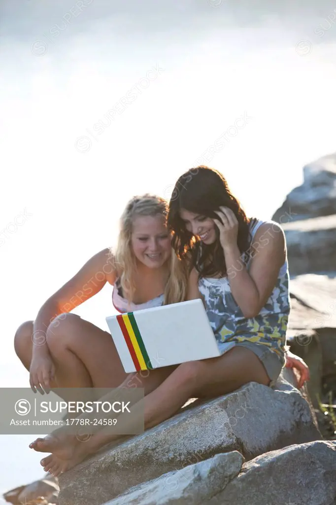 Two young women laugh while looking at pictures on a computer next to the lake.