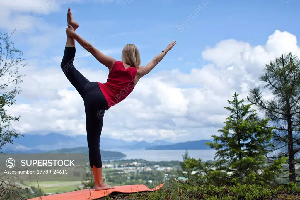 Young woman does yoga in nature overlooking a large lake.